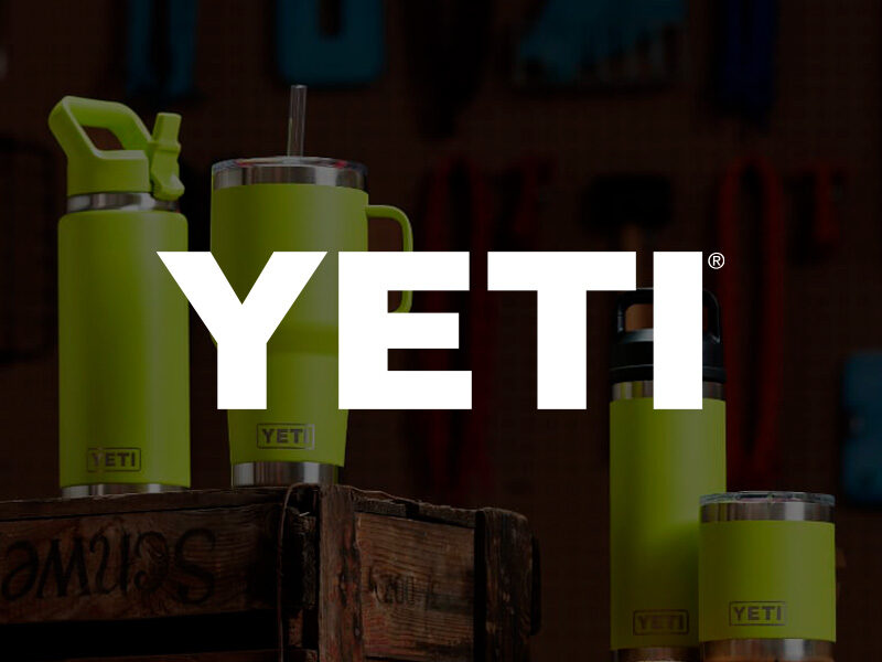 Yeti logo over and image of five bright yellow Yeti drink wares stacked on wood cartons with tools in the background.
